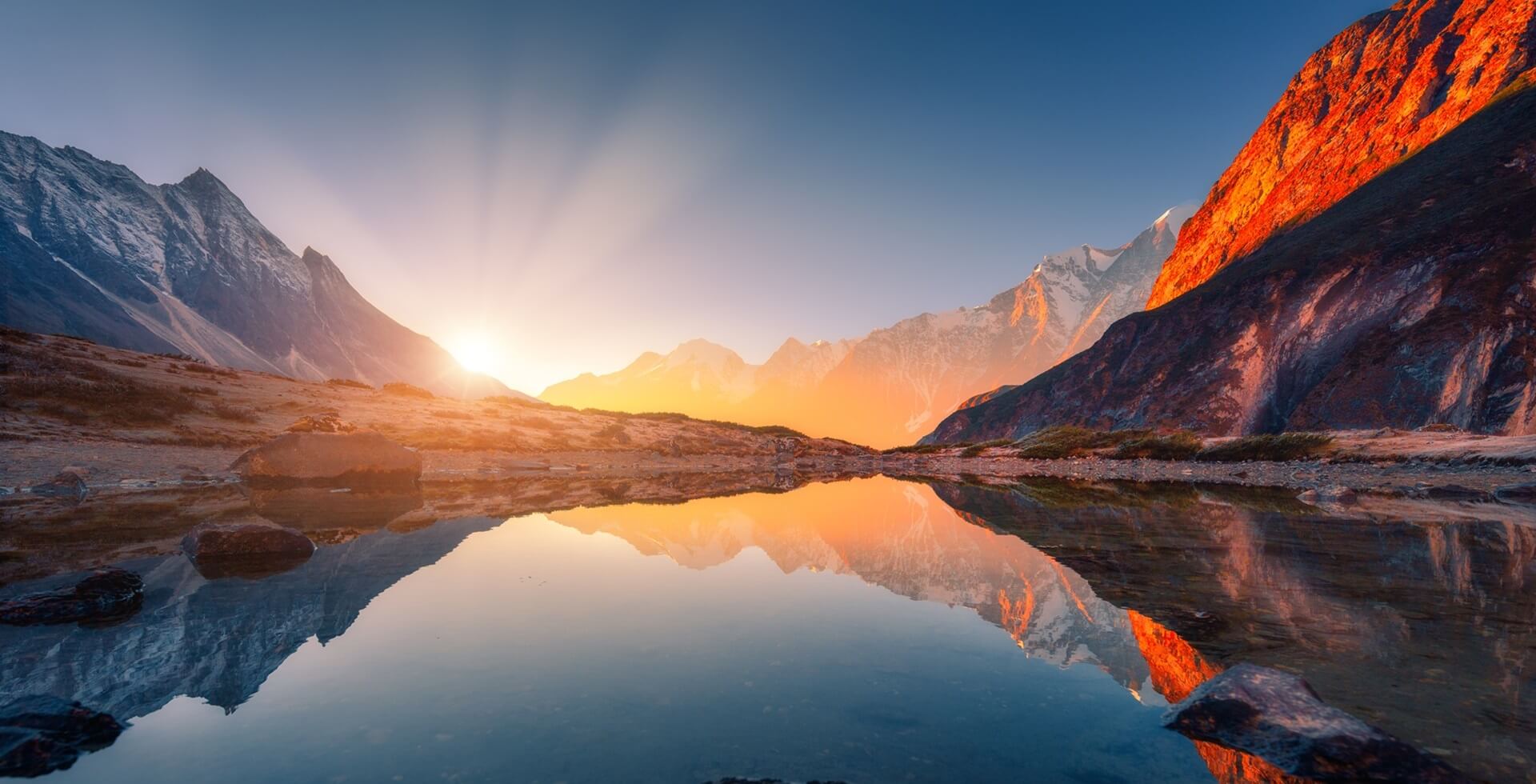 Footer Bela paisagem com altas montanhas com picos iluminados, pedras no lago de montanha, reflexão, céu azul e luz solar amarela no nascer do sol. Nepal