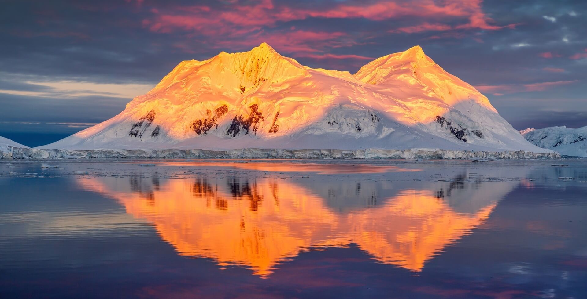 Footer Mountain with red orange top light up by midnight sun with reflection in the sea in Antarctica