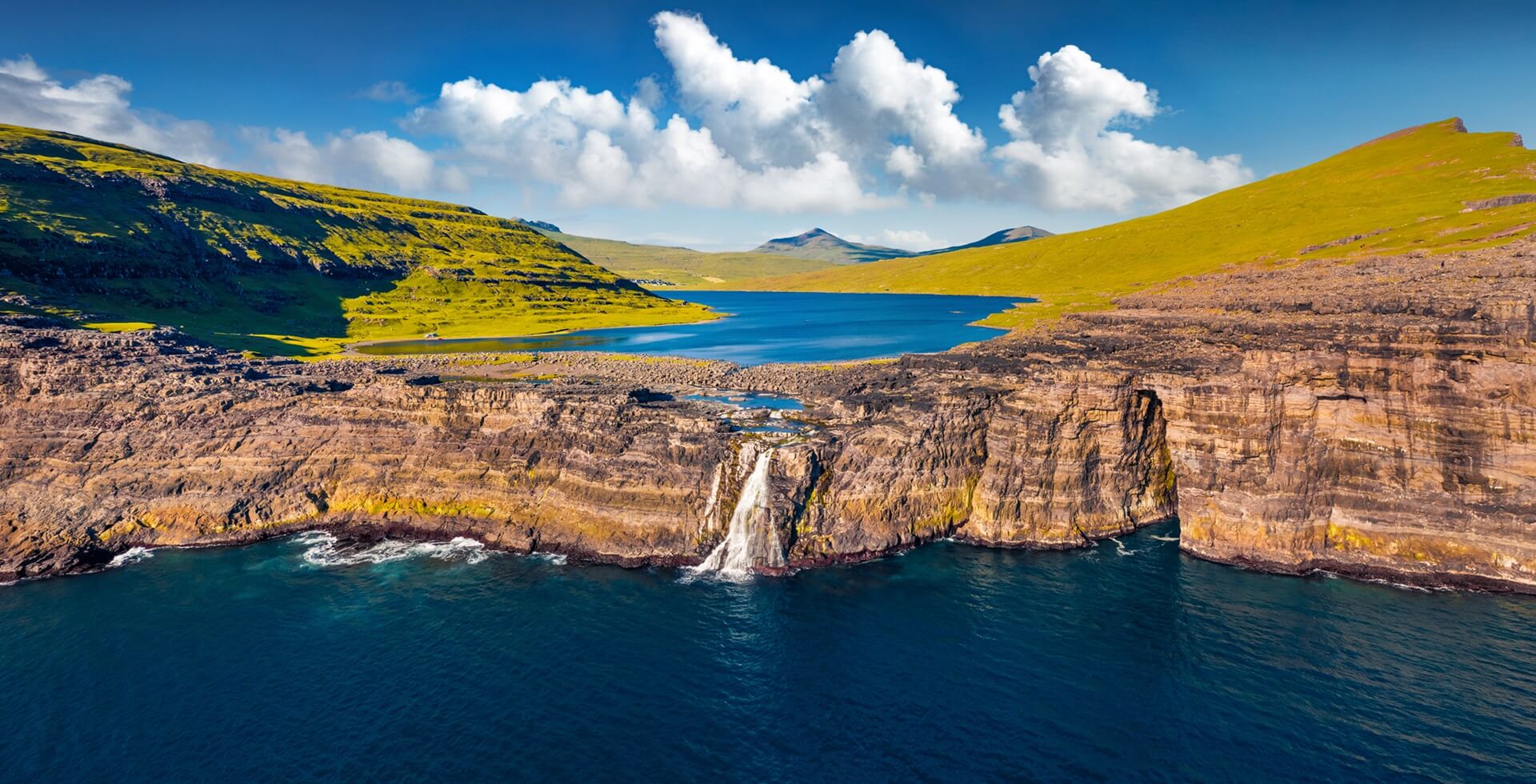 Footer iew from flying drone. Panoramic morning view of Bosdalafossur waterfall, that falls directly into the ocean. Exciting summer scene of Sorvagsvatn lake, Vagar, Faroe Islands,