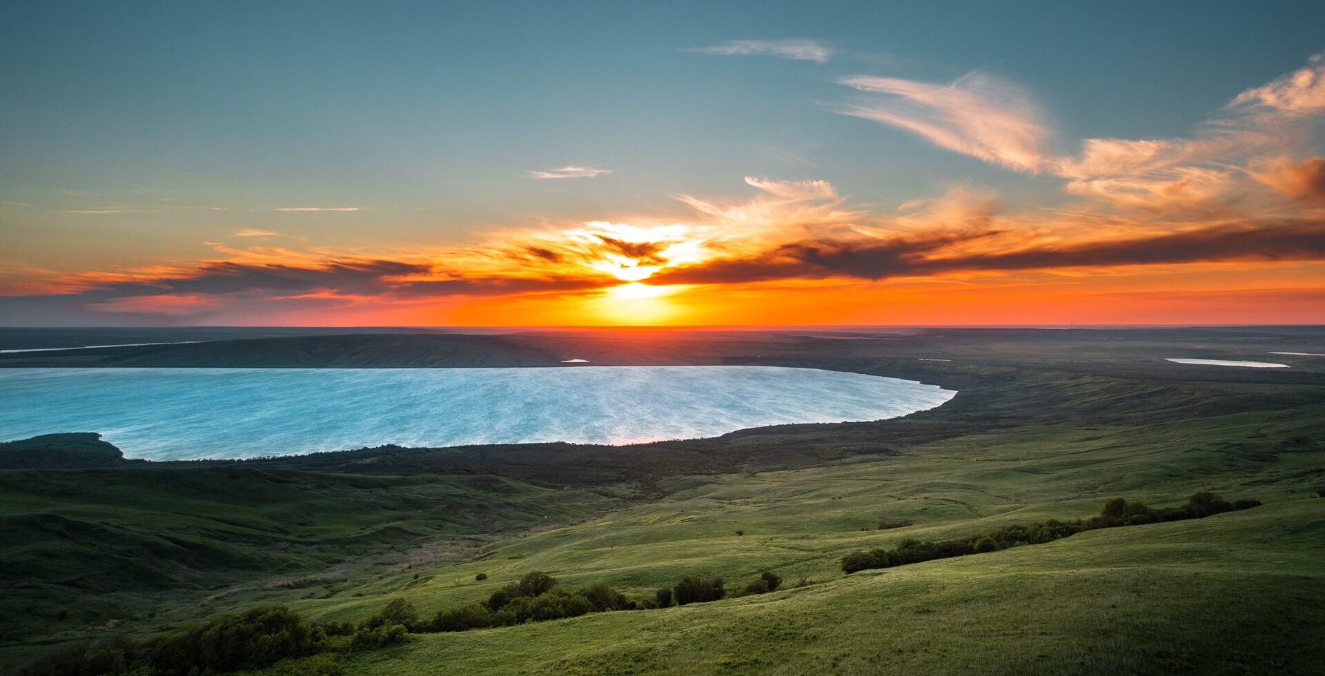 Footer picturesque lake surrounded by a green meadow in the rays of the setting sun